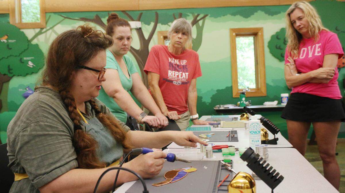 Artist Tara Tonsor demonstrates how to solder stained glass as Amanda Wood, Sandra Campbell and Erika Jump watch during a class at the Overland Park Arboretum.