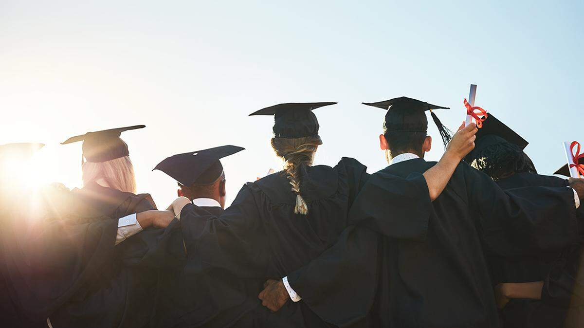 Rear view shot of a group of university students standing outside on college graduation day PeopleImages