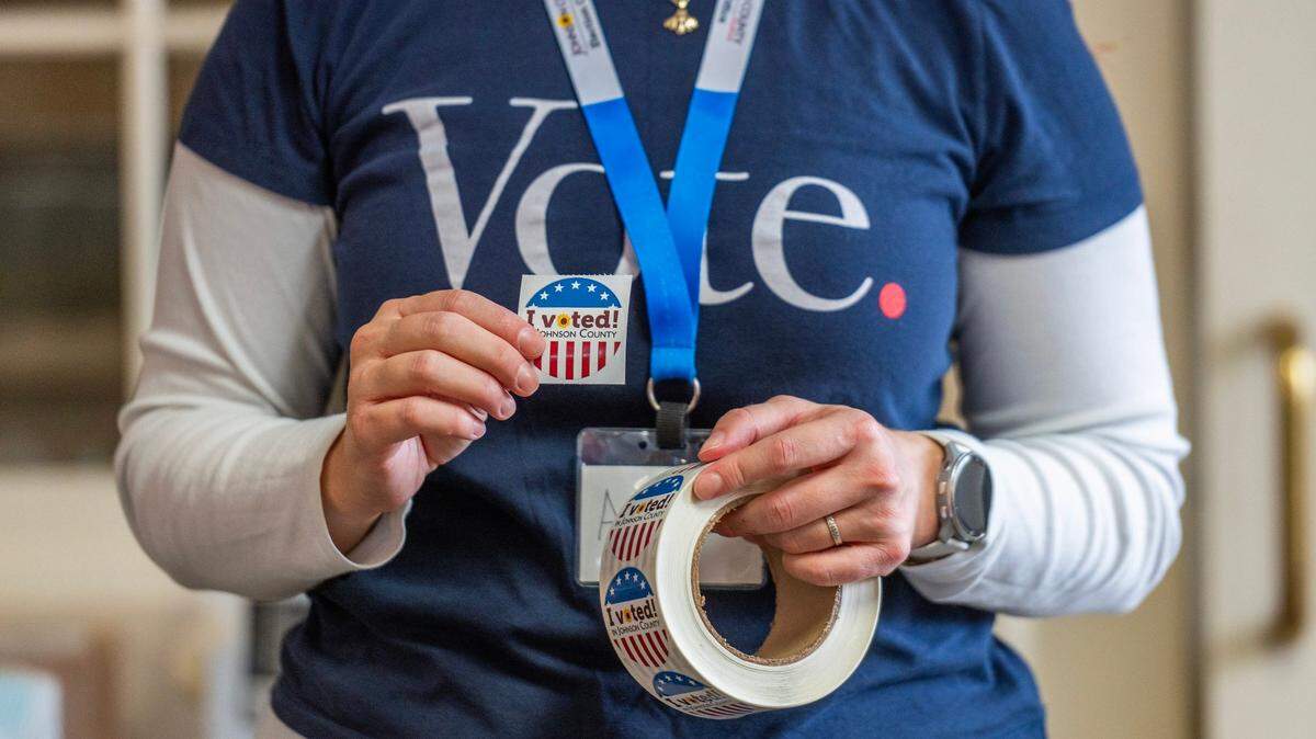 A polling volunteer holds an ‘I Voted’ sticker while waiting for voters to cast their ballots in Prairie Village in 2023.