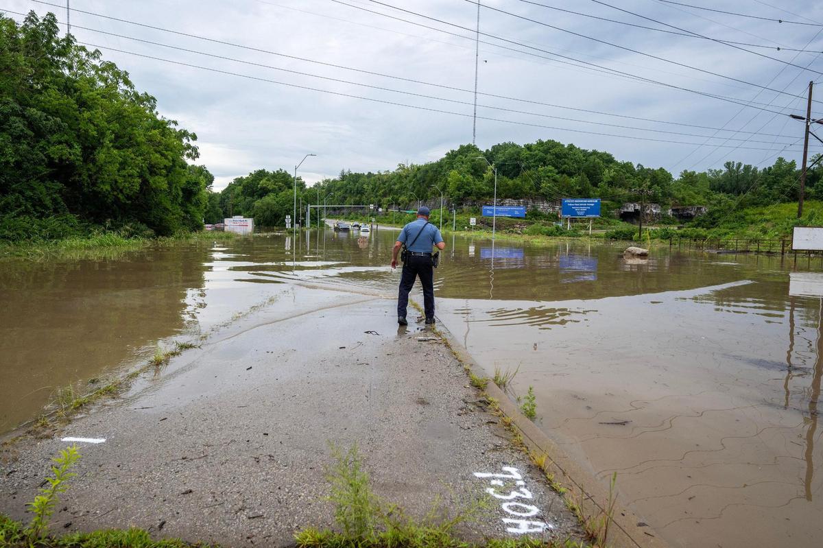 A Kansas City police officer surveys flooding along East 23rd Street on Thursday, July 17, 2025, in Kansas City. Markings on the pavement by the Missouri Department of Transportation indicate the height of floodwaters after heavy overnight rainfall inundated the area.