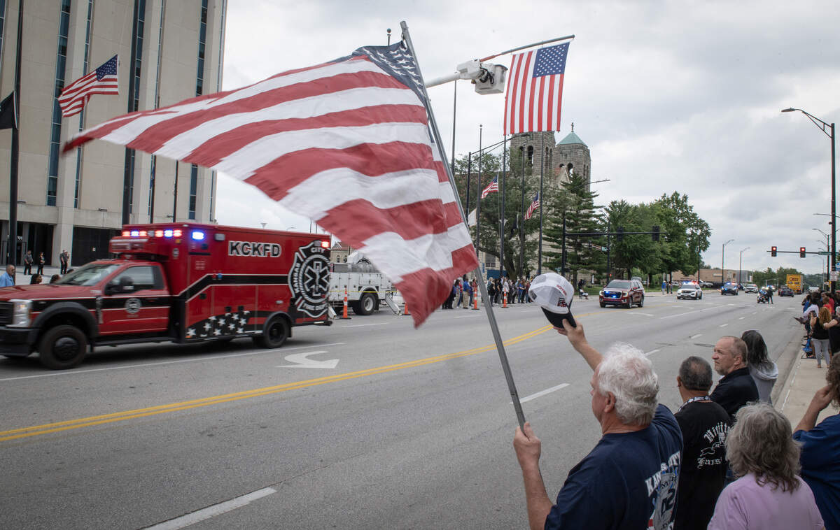 Michael Hoffman, father of slain KCMO firefighter Graham Hoffman, held onto a flag and tipped his hat to first responders while he watched the funeral procession for Wyandotte County Sheriff's deputy Elijah Ming pass through downtown Kansas City, Kansas, on Monday, August 11, 2025.