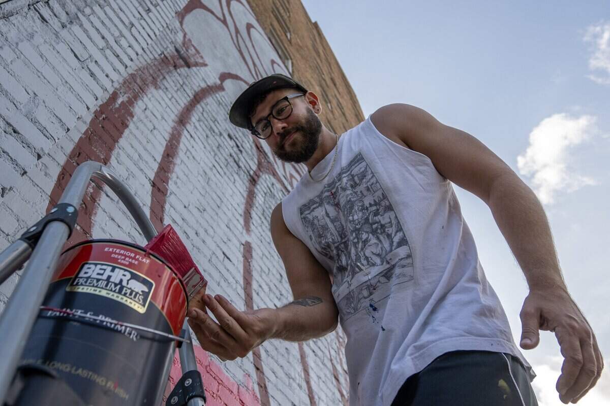 Artist Jared Horman dips a paintbrush into a can of pink paint while working on a Chappell Roan mural along Broadway Boulevard on Wednesday, Sept. 24, 2025, in Kansas City.
