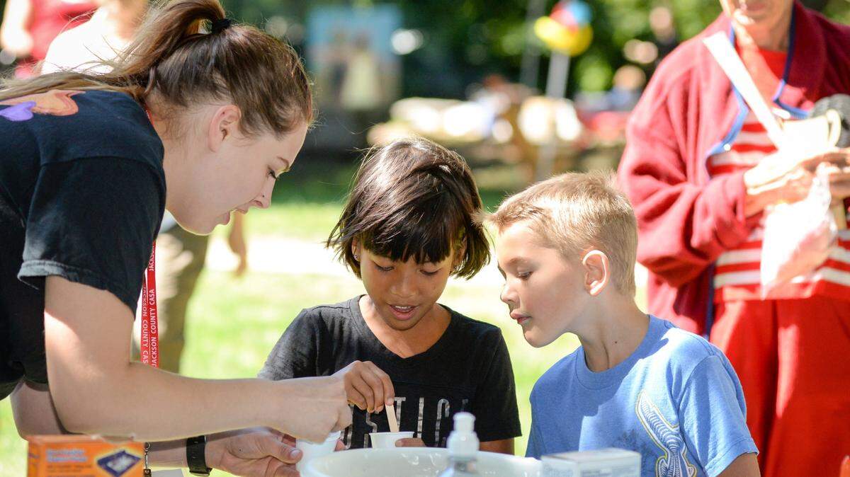 At a pre-pandemic CASA carnival, Liz the Science Whiz shows Sophie Purcell and Jacob Purcell a small science experiment.