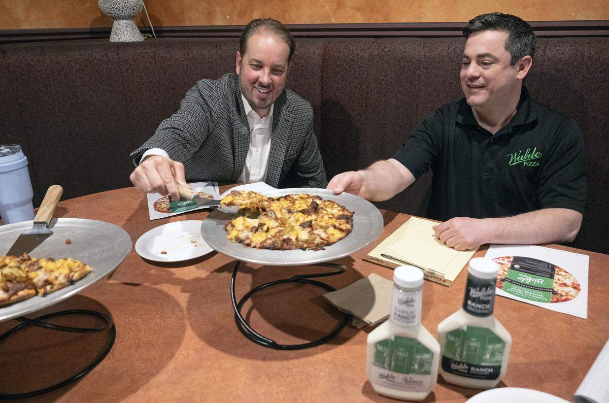 Aaron Kanatzar, right, general manager of Waldo Pizza, looks on as Whitney VinZant, chief executive officer of W. VinZant Restaurants, tries a slice of a new pizza featuring Jack Stack Barbecue.