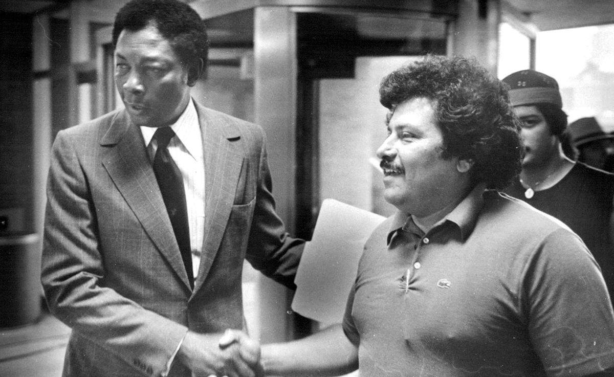 West side leader Don Pecina (right) and Kansas City School Superintendent Robert Wheeler confirm the agreement to turn the West Business/ Management Center into a community school in 1981.
