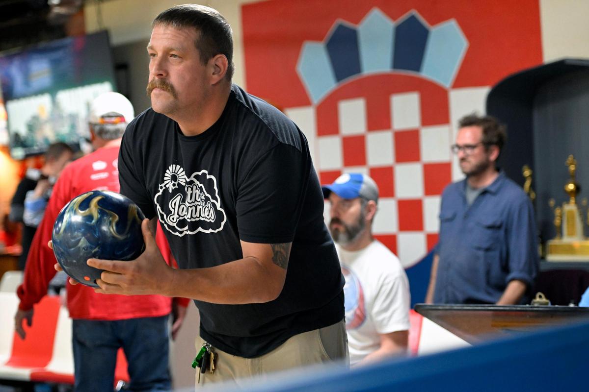 A Croatian crest adorns the wall behind Mike Peterson as he prepares to send his bowling ball down the lane during the Monday night league at St. John Catholic Club. 