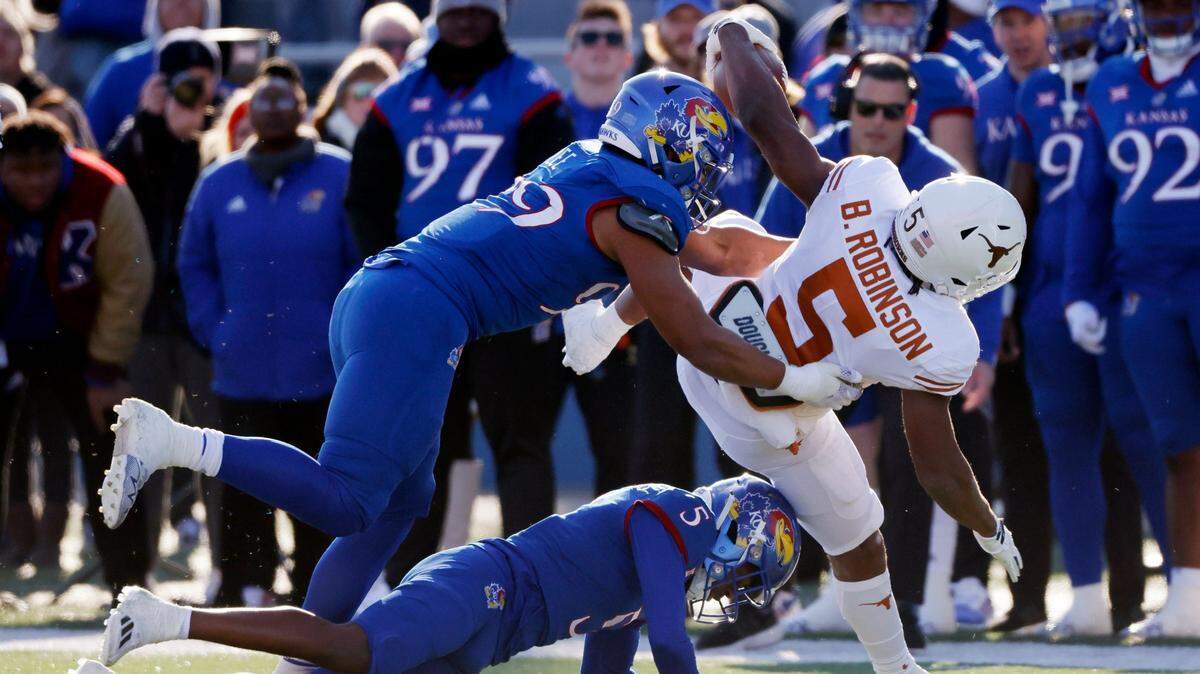 Texas running back Bijan Robinson rushes for a first down as Kansas defensive lineman Malcolm Lee (99) and safety O.J. Burroughs (5) make the stop on Saturday, Nov. 19, 2022, in Lawrence, Kan.