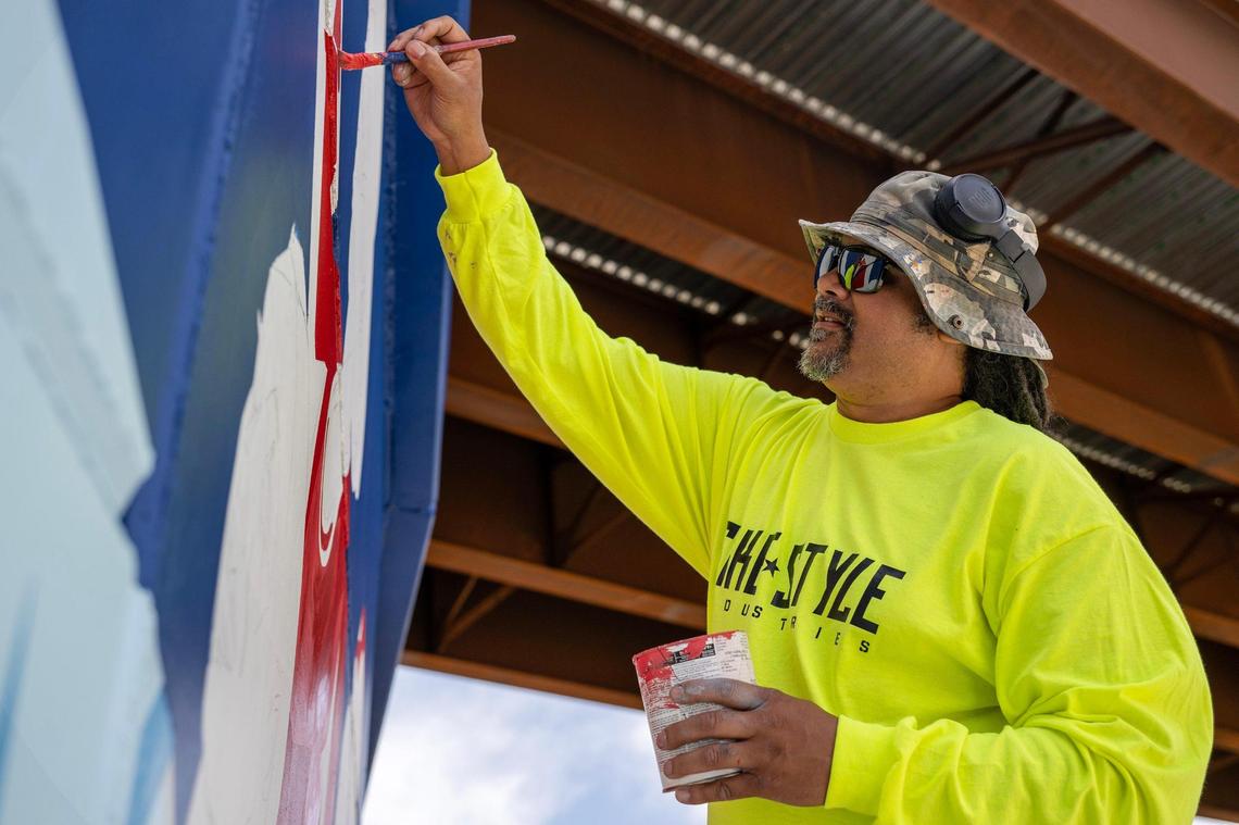Phil Shafer uses a small paintbrush to add detail to a mural he designed commemorating the new Buck O’Neil Bridge near the intersections of Broadway Boulevard and West 3rd Street.