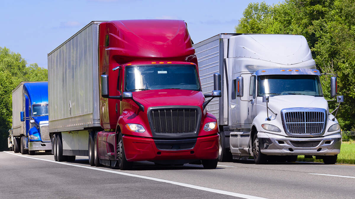 Horizontal shot of red, white, and blue trucks on an interstate with copy space. Heat waves rising from the hot asphalt creates a blurring effect on background trucks and foreground pavement.
