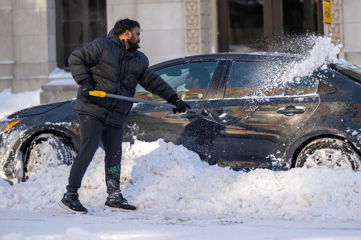 A resident helps a driver clear snow around their vehicle stuck in a parking spot along Armour Boulevard on Monday, Jan. 6, 2025, in Kansas City.