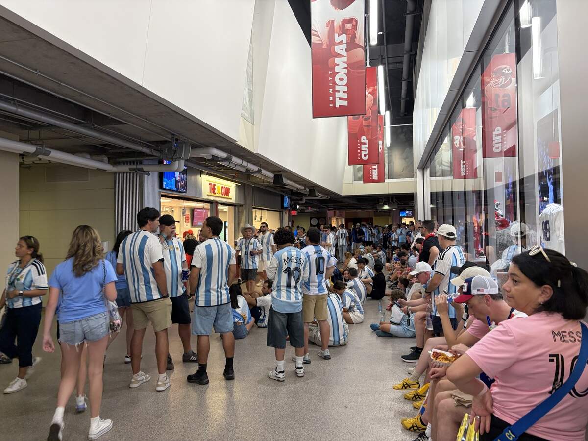 A group of Argentina fans gathering around one of the lower level concourse TVs watching the end of the Norway vs. England match.