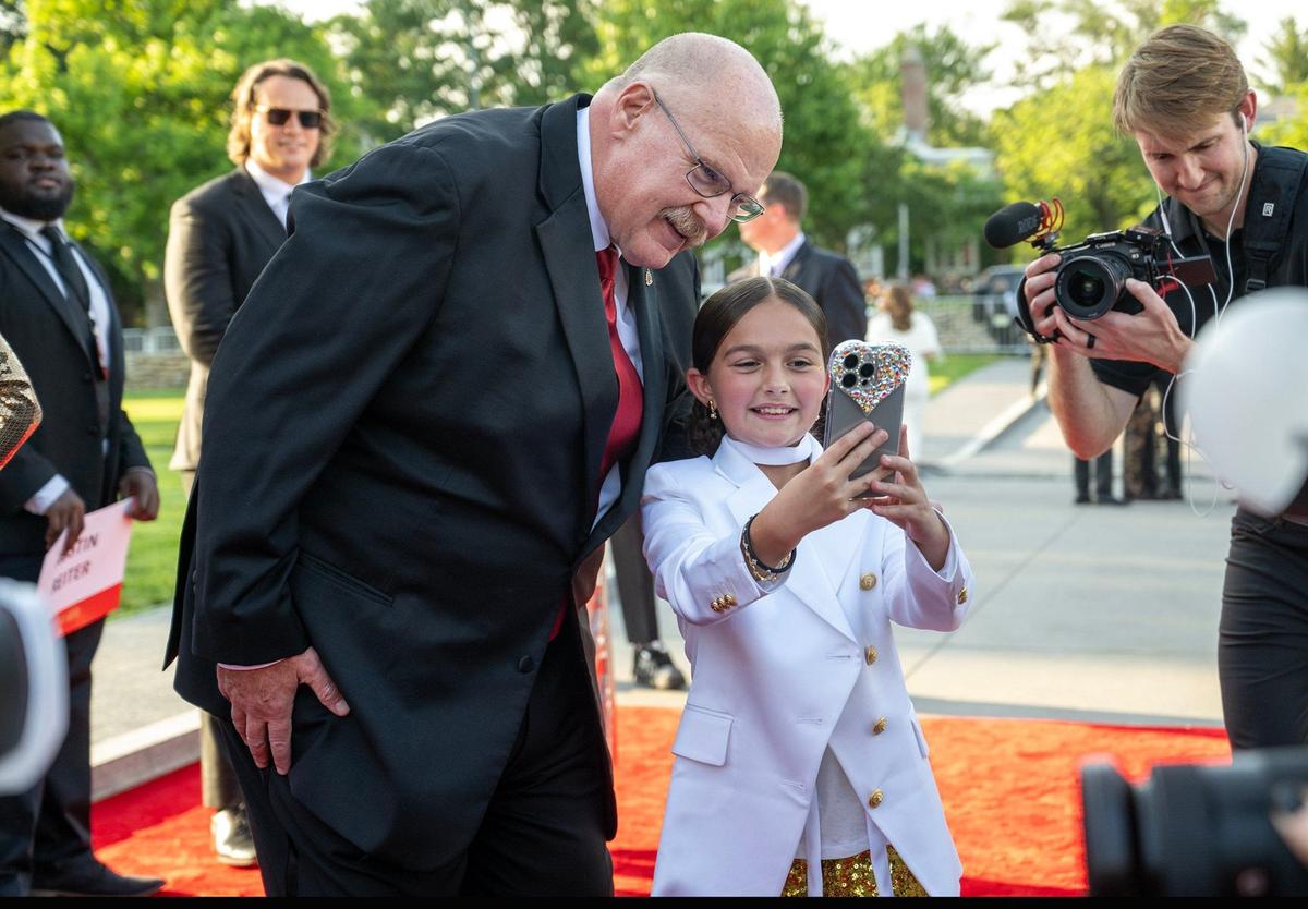 Chiefs Head Coach Andy Reid took a selfie with Taylen Biggs, a social media personality, as he walked the red carpet before the Super Bowl LVIII championship ring presentation event.