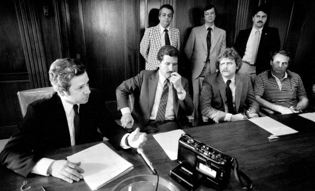 Mayor Richard L. Berkley, left, relates the outcome of closed meetings to reporters in 1984. Seated, from left; City Manager A.J. Wilson, John Tvedten, chief negotiator for Local 42 of the International Association of Fire Fighters, and Robert Palmer, secretary-treasurer of the local. Standing in the background are other union members.