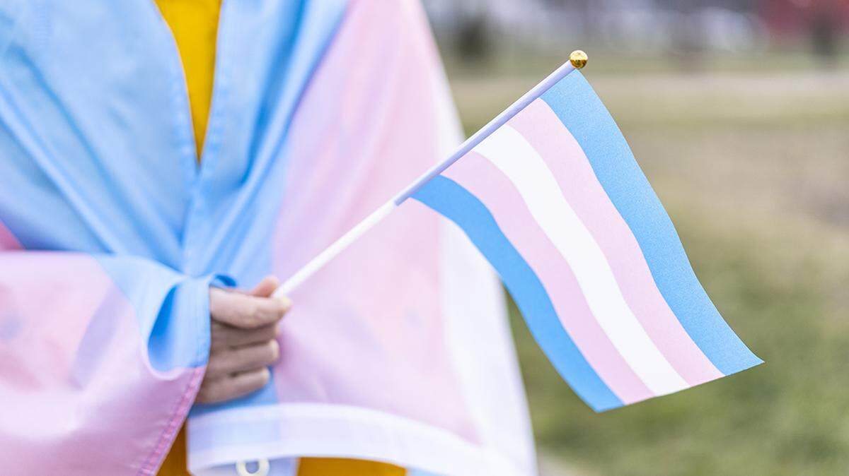 Transgender covered with the transgender flag and holding a flag in the hand for defending her rights