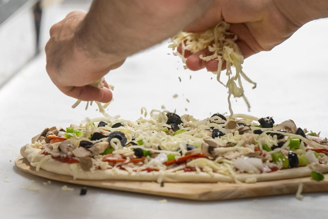 Cheese is sprinkled onto a pizza during the grand opening of Pizza 51’s newest location in Olathe on Wednesday, June 25. They serve slices, calzones, sandwiches, and salads.