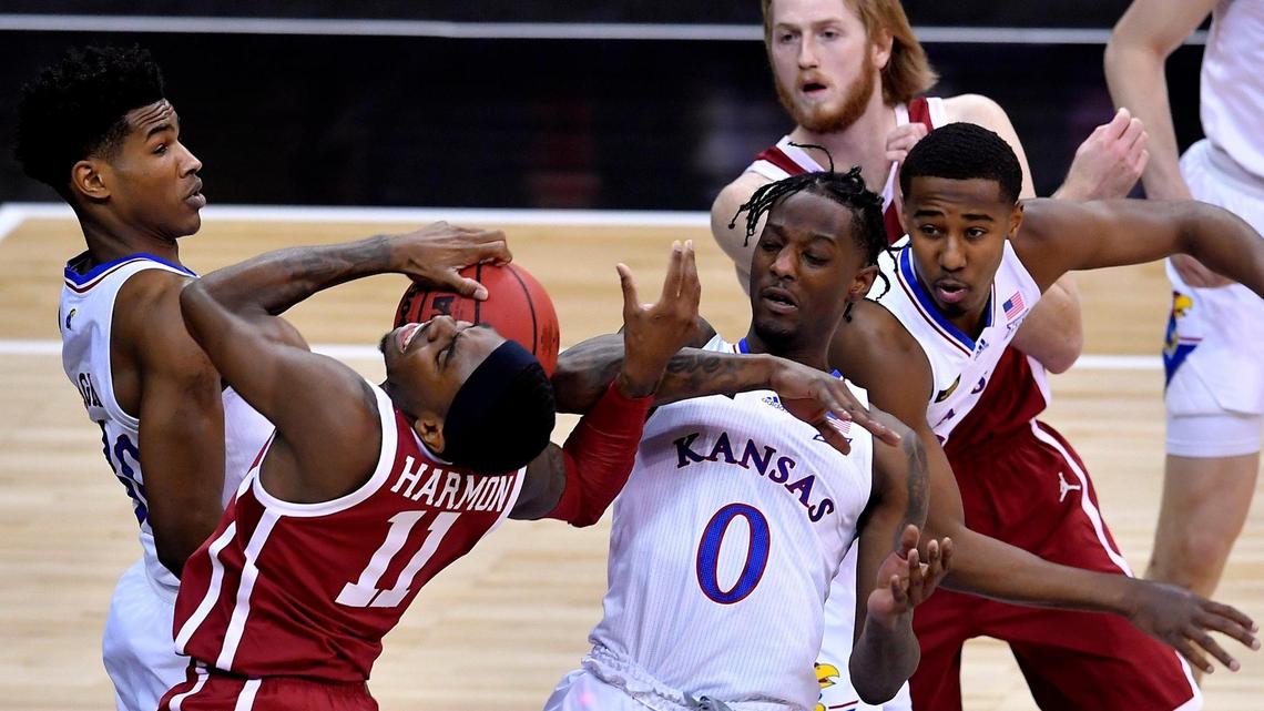 OU’s De’Vion Harmon (in red, left) tangles with KU’s Ochai Agbaji (left) and Marcus Garrett as they battle for a rebound during the first half of a game at the Big 12 Tournament earlier this year.