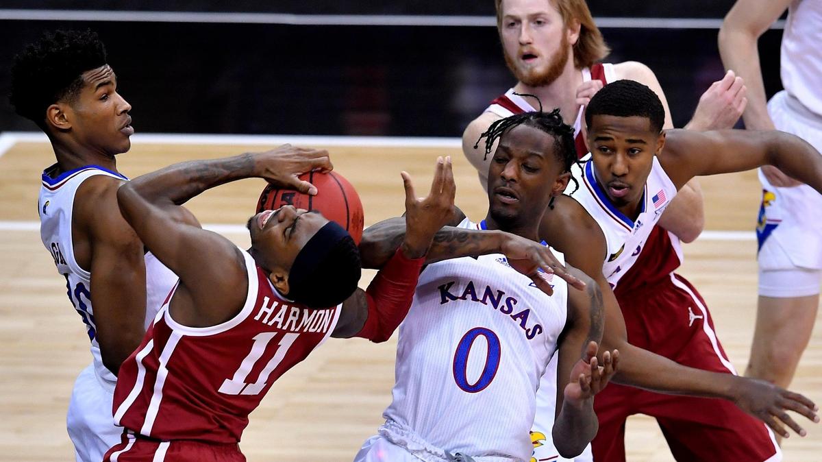 OU’s De’Vion Harmon (in red, left) tangles with KU’s Ochai Agbaji (left) and Marcus Garrett as they battle for a rebound during the first half of a game at the Big 12 Tournament earlier this year.