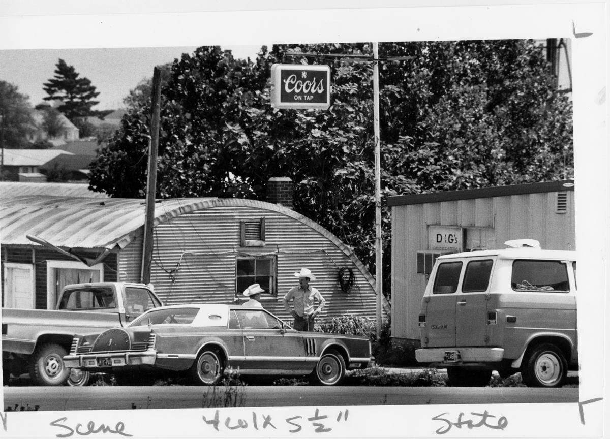 Two residents of skidmore, Missouri, chat in front of the tavern where Ken Rex McElroy was slain. Bullet holes were found in the wall of the corrugated metal building on the left.