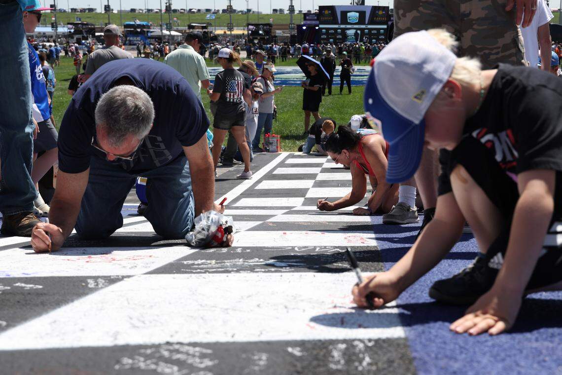 Fans sign the finish line during a pre-race “track walk” that took place ahead of the Sunday, May 11, 2025 AdventHealth 400 auto race at Kansas Speedway in Kansas City, Kan.