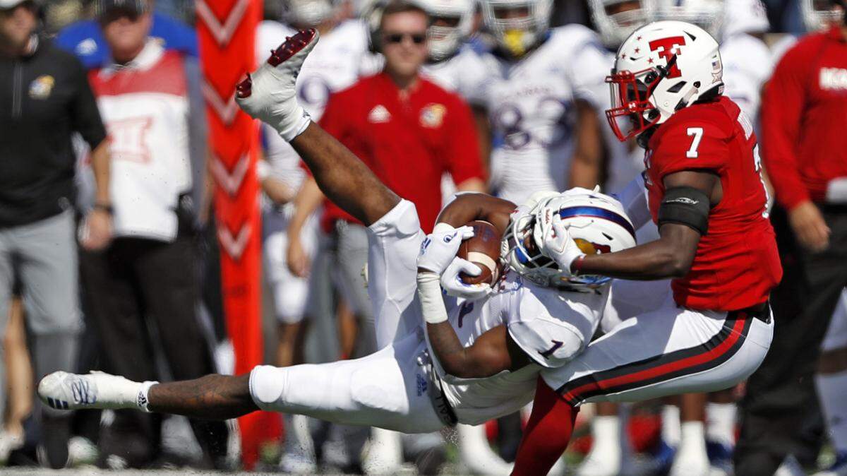 Kansas’ Pooka Williams Jr. (left) was tackled by Texas Tech’s Jah’Shawn Johnson during the first half on Saturday in Lubbock, Texas.