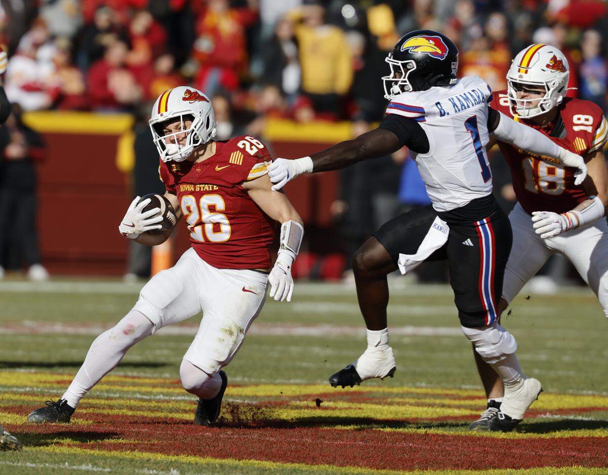 Carson Hansen #26 of the Iowa State Cyclones rushes for yards as Bangally Kamara #1 of the Kansas Jayhawks defends in the first half at Jack Trice Stadium on November 22, 2025, in Ames, Iowa.
