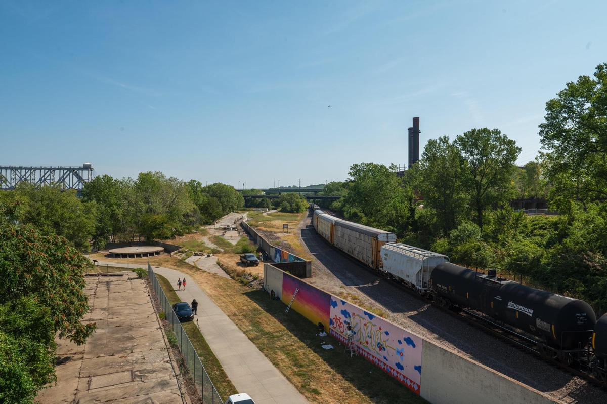 A train passes by a wall of murals being created along the Riverfront Heritage trail on Friday, Sept. 15, 2023, in Kansas City. Port KC commissioned local and national artists to create murals along the concrete wall to beautify the area and to deter vandalism.