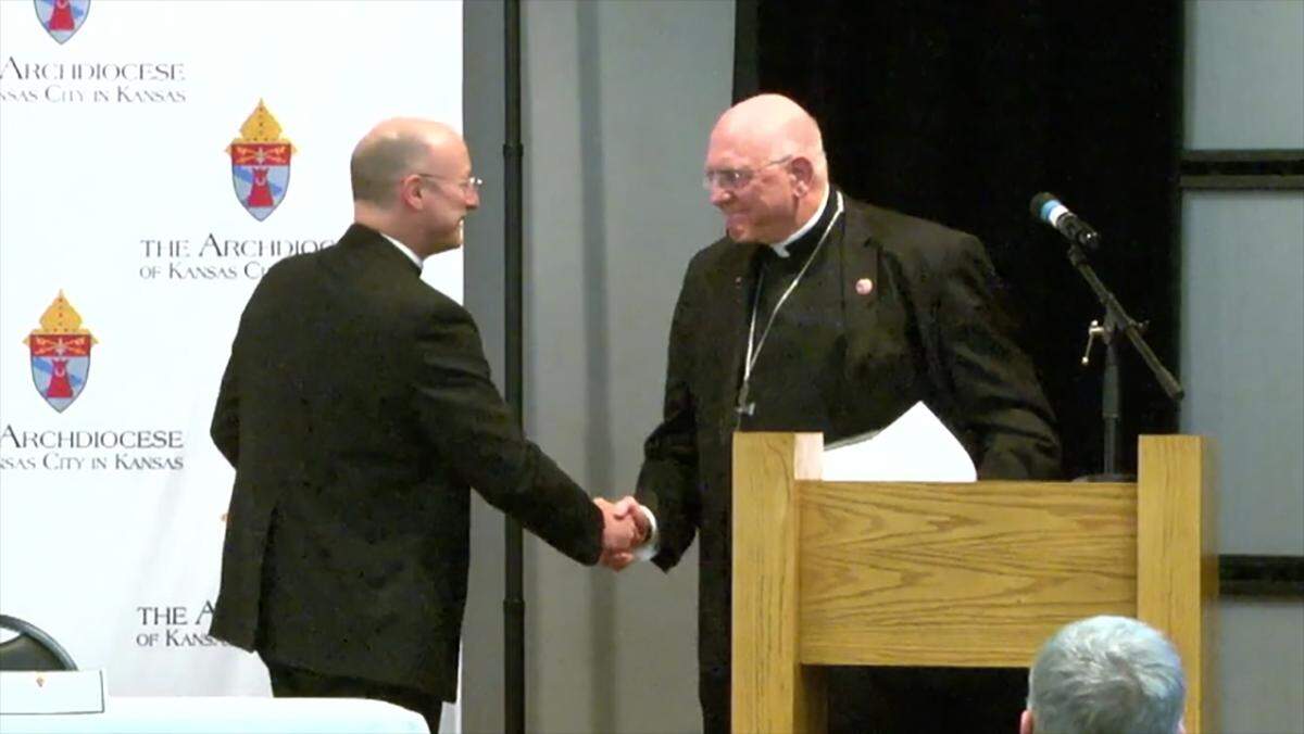 Archbishop Shawn McKnight, left, shakes hands with outgoing Archbishop Joseph Naumann