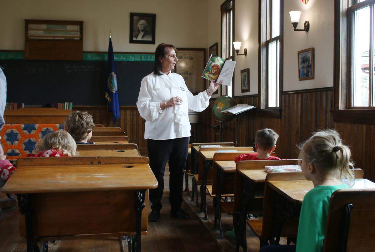 Children listen to Linda Van Coevern, an educator at the Deanna Rose Children’s Farmstead, read a story in the site’s one-room schoolhouse.
