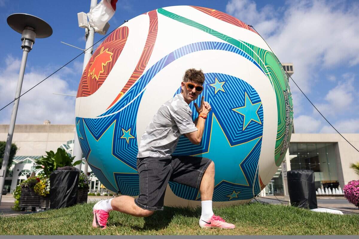 Oliver Wright poses next to the inflatable World Cup soccer ball showing off their pink cleats at Crown Center on Sunday, June 28, 2026. He’s known online as “Side Quest Dad,” and is a 34-year-old British content creator who has lived in Kansas City for the past 15 years and shares everyday adventures with his followers through social media. He recently gained local attention after a viral video warning World Cup visitors about Midwest summer weather.