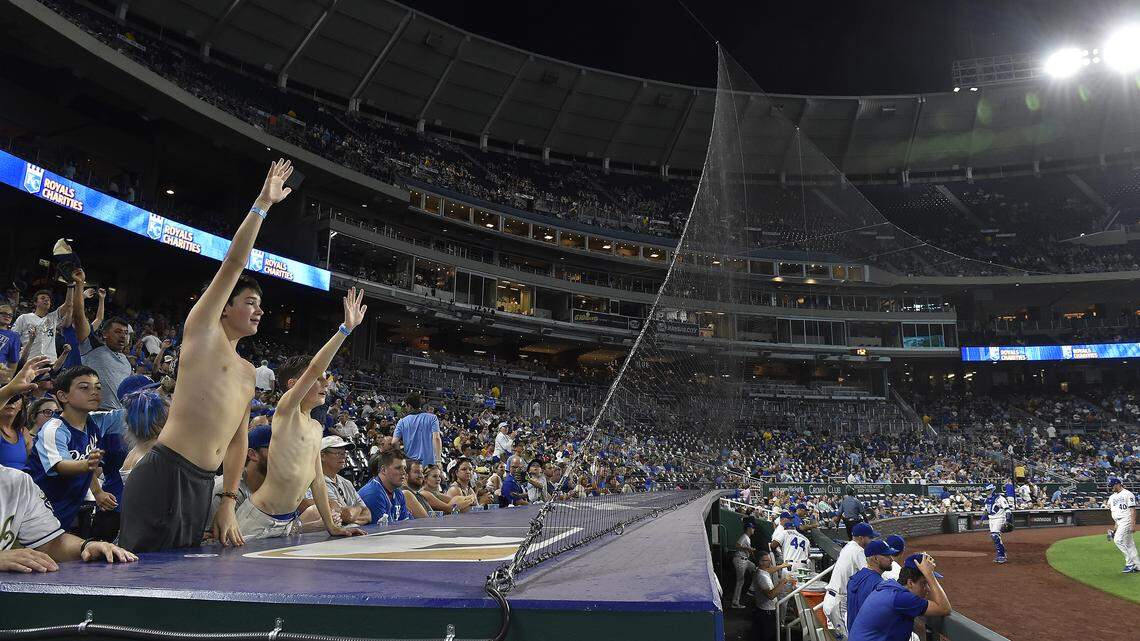 Royals fans behind the netting at Kauffman Stadium try to get the attention of players coming off the field.