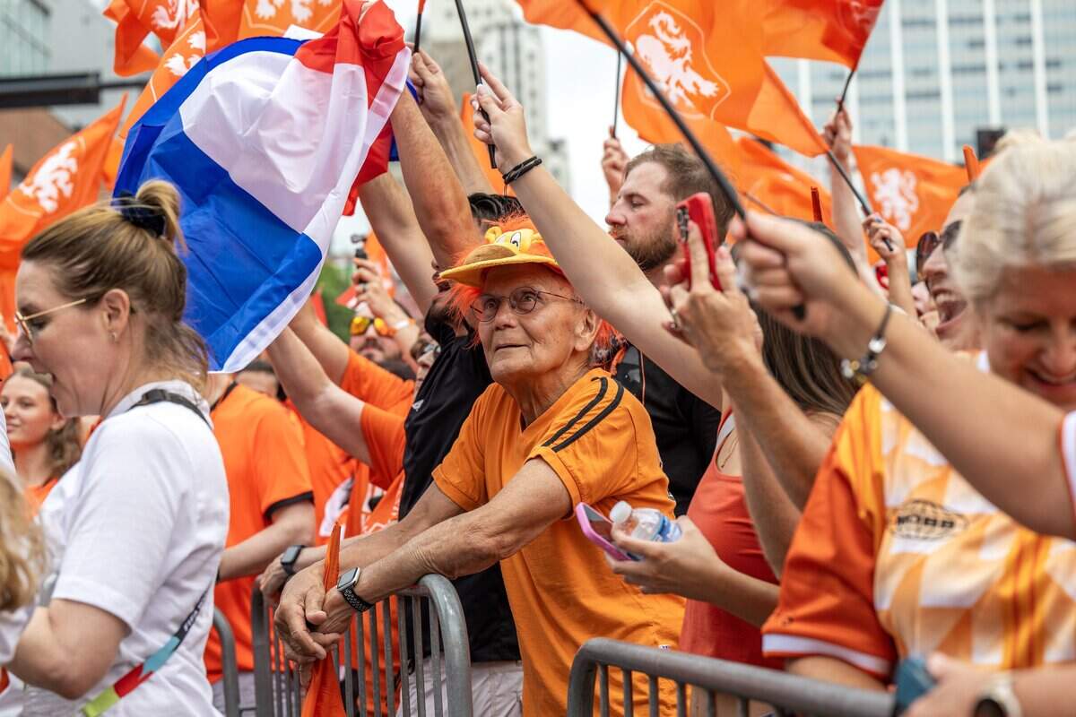 Fans wave flags during the Orange Walk as a fan watches from behind a barricade on Thursday, June 25, 2026, in Kansas City.
