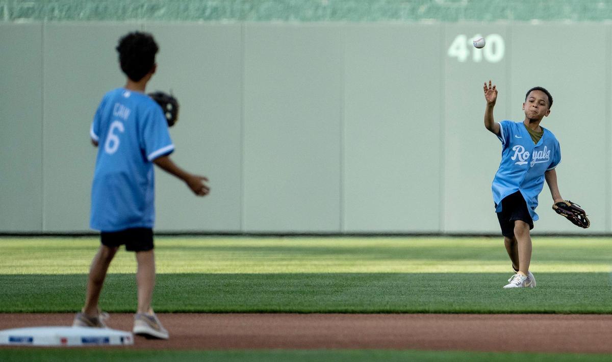For the ceremonial first pitch, Jayden Cain, right, throws a ball to his brother, Cameron, as they relay a ball from center field to their dad and former Kansas City Royals center fielder Lorenzo Cain during a retirement ceremony at Kauffman Stadium on Saturday, May 6, 2023, in Kansas City. Cain signed a ceremonial one-day contract to retire as a Royal.