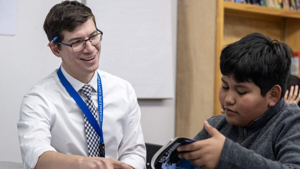 Christopher Leavens, an English language development teacher at Guadalupe Centers Middle School, talks with Alan, a seventh grade student who looks over a library book, during class on Thursday, Dec. 4, 2025, in Kansas City. Since the school has no library, Leavens has started a small library in his classroom.
