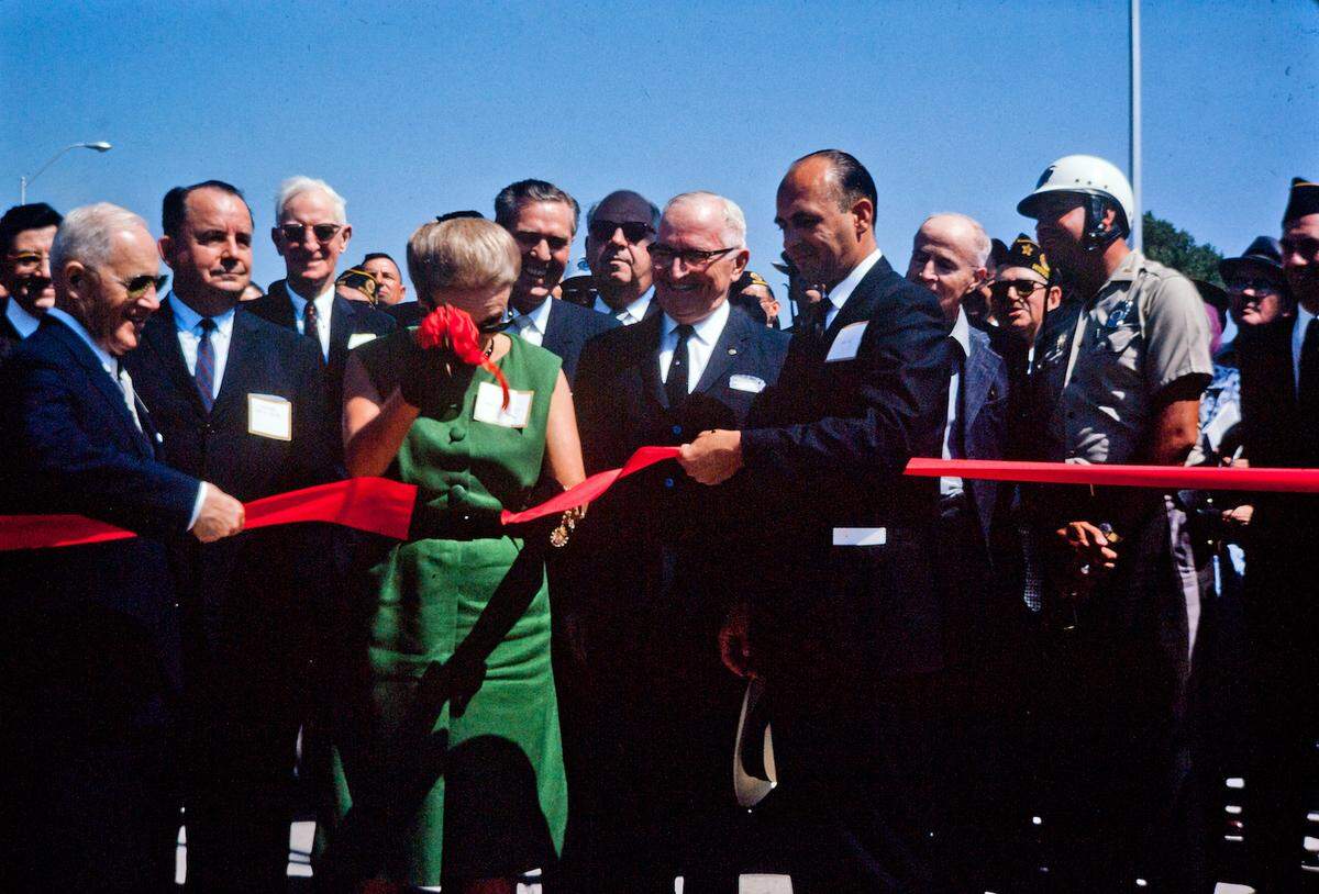Photo of Callie Whitton, wife of Federal Highway Administrator Rex M. Whitton, cutting the ribbon to open the new Southeast Freeway with the assistance local mayors and President Truman, 1962. 