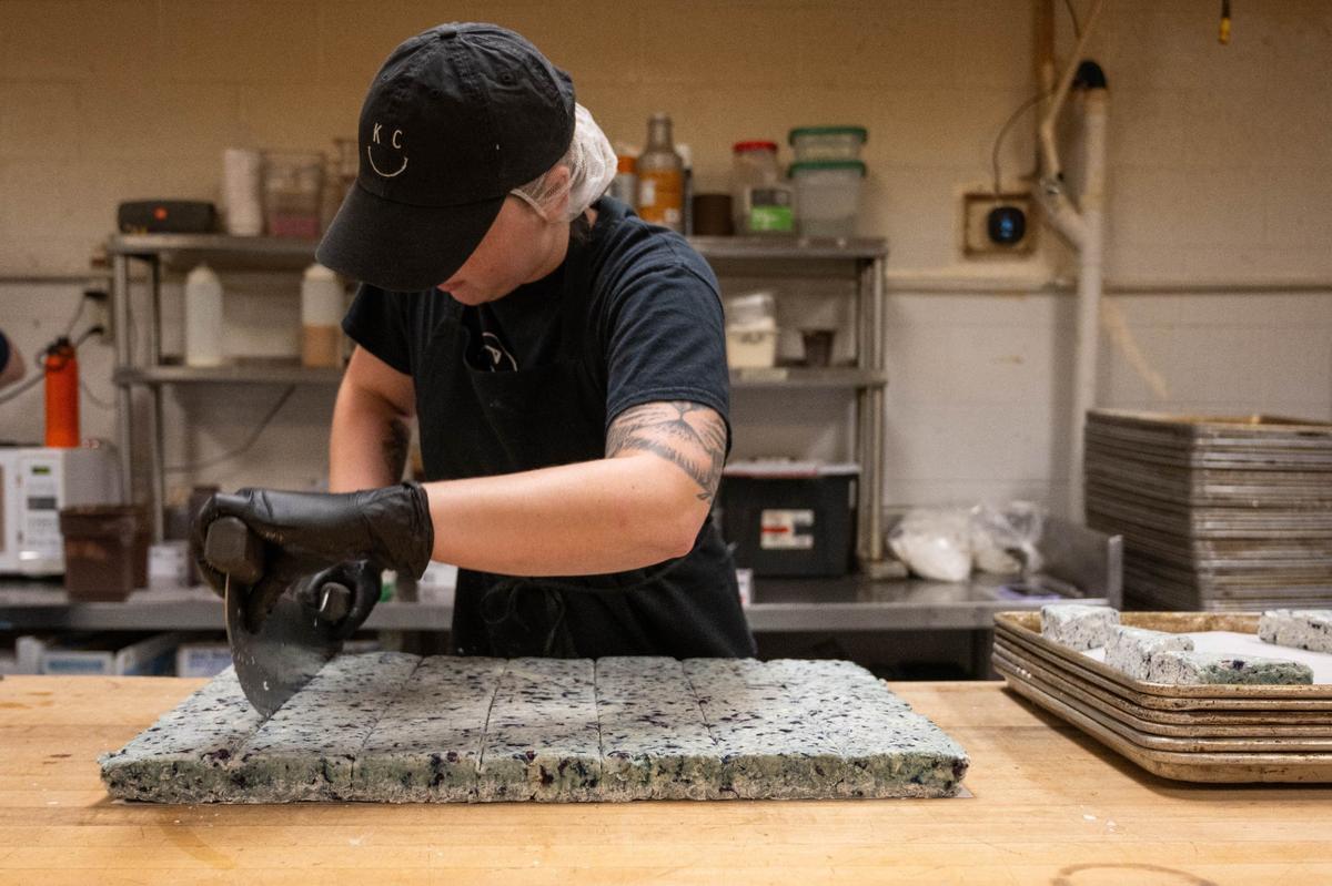 Haleigh Trumpp, a baker at Scratch KC, slices a sheet of blueberry scone dough. The dough is laid out in a sheet and sliced into individual scones, baked, and then glazed.