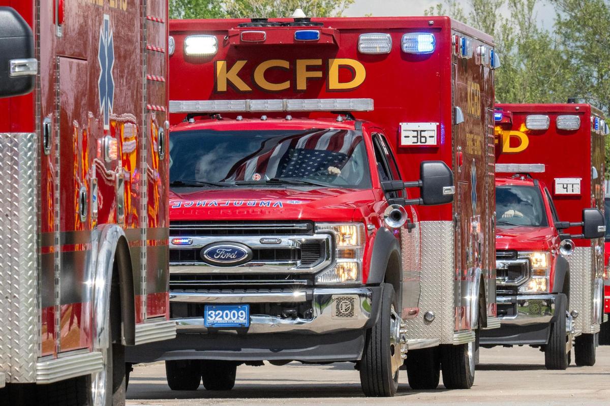 Kansas City Fire Department ambulances pass beneath a large American flag suspended between ladder trucks during a funeral procession for Graham Hoffman on Friday, May 2, 2025, in Liberty.