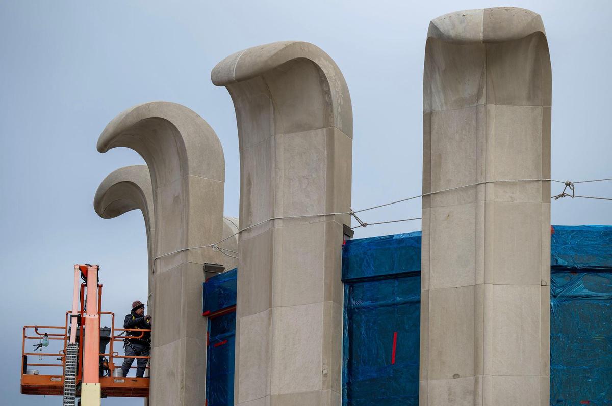 Haris Henriquez of MTS Contracting, Inc., based in North Kansas City, applies a blue plastic film to the windows during renovation work on the curved concrete pillars of the building at 8101 Lenexa Drive, in Lenexa on Thursday, Jan. 2, 2024. Originally built in 1968 for $3.2 million for Eisen Mercantile Inc., the building features outward-curving pillars resembling flower petals.