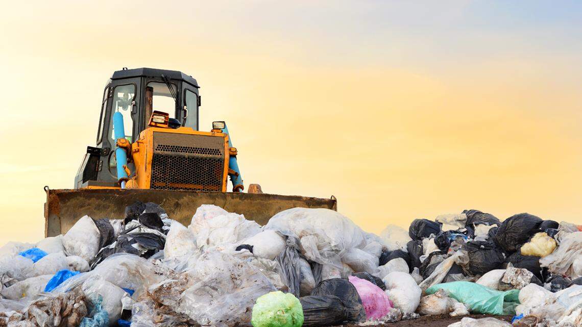 Garbage dump with plastic bags and food waste. Recycling of construction waste on junk yard. Refuse collection. Bulldozer dispose of rubbish at a landfill. Trash disposal area. Dozer on rubbish dump