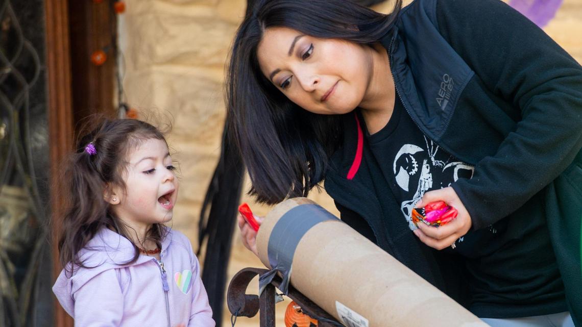 Mariana Sanchez, 2, asks her mother, Liliana Sanchez, to throw candies through a DIY candy chute to her brother Rafael (not pictured) while they set up Halloween displays outside their house in Coleman Highlands neighborhood of Kansas City on the afternoon of Oct. 31. This year, candy chutes have been a popular choice for many families as a safe way to give out candies to trick-or-treaters.