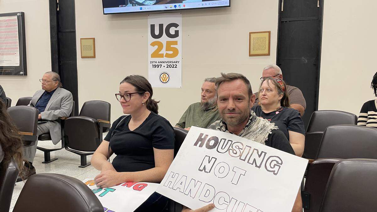 A resident attending a Unified Government meeting holds up a sign reading “Housing Not Handcuffs” on Oct. 2, 2025.