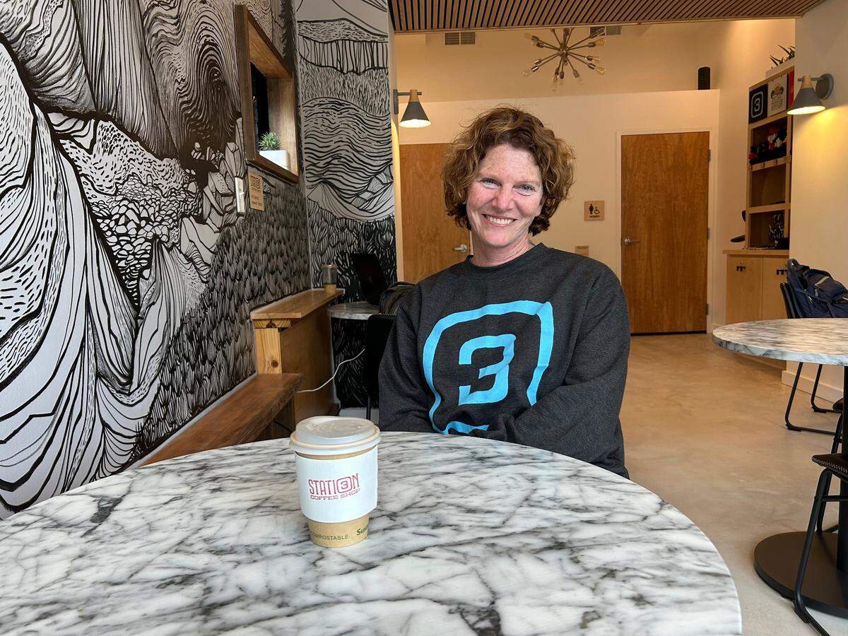 Courtney Nelson owns Station 3 Coffee. A mountainous mural, painted in honor of her son, a climber, is seen behind her.