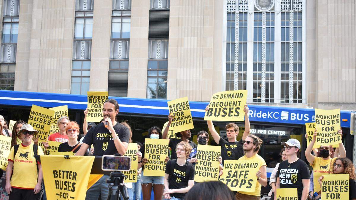 A city bus passes behind activists with the Better Buses for KC campaign as activist Anthony Cunningham speaks in front of Kansas City Hall on Thursday, Sept, 21, 2023.