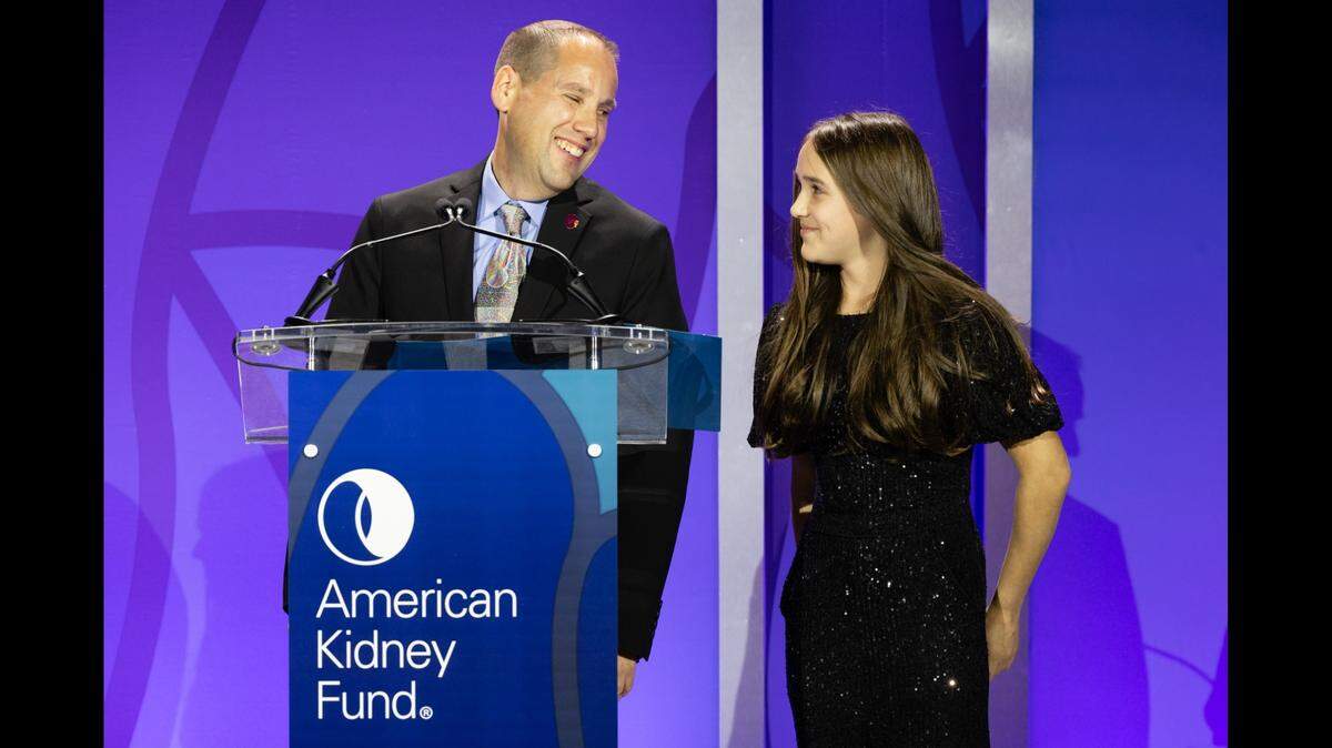 Todd Ehrlich stands on stage with his daughter Hannah as she is honored for her artwork at the American Kidney Fund’s annual gala in Washington, D.C.