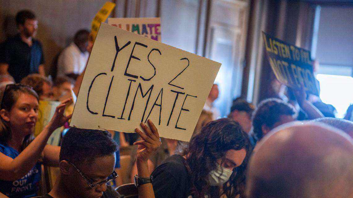 Climate protection supporters held up signs during Kansas City’s Transportation, Infrastructure and Operations Committee meeting at Kansas City Hall on Wednesday, Aug. 24, 2022. The committee was voting on a resolution regarding the city’s new climate plan.