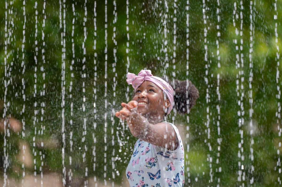 Eleven-year-old Jazya Avery tests the warmth of the water before walking through the fountain at the Sprayground in Gillham Park on Monday, July 18, 2022. Kansas City is expected to see temperatures as high as 100 degrees or above for several days this week.