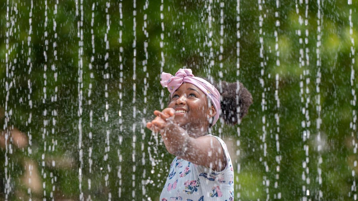 Eleven-year-old Jazya Avery tests the warmth of the water before walking through the fountain at the Sprayground in Gillham Park on Monday, July 18, 2022. Kansas City is expected to see temperatures as high as 100 degrees or above for several days this week.