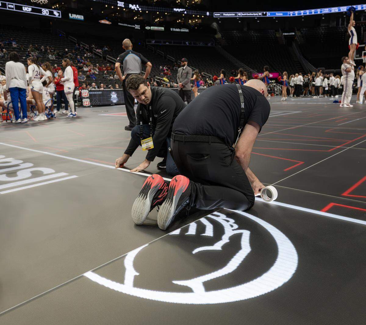 Arena crew members place white tape on the court after LED lights malfunctioned following the third quarter of a game between the Kansas Jayhawks and the UCF Knights of the Big 12 Women's Basketball Tournament at T-Mobile Center on Wednesday, March 4, 2026, in Kansas City.