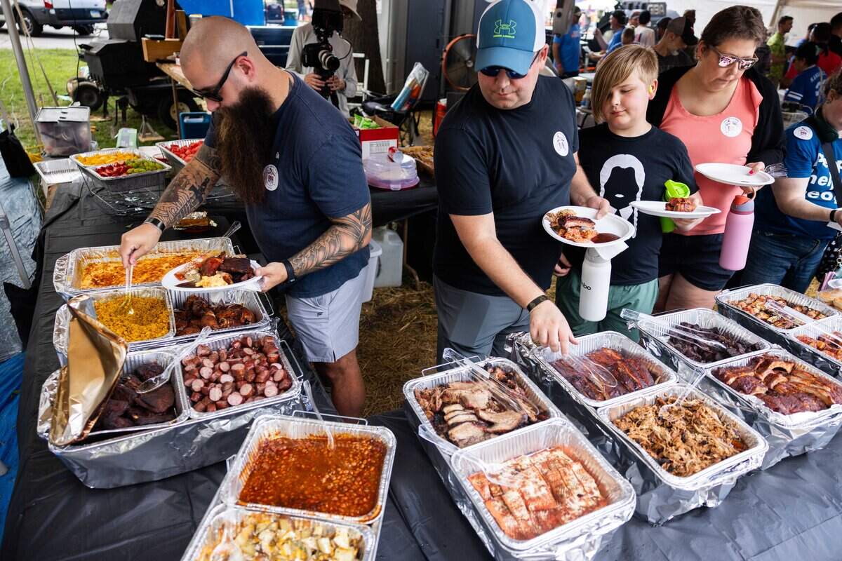 A group of guests rotate around tables lined with trays of food filling their plates at The Great Lenexa BBQ Battle on Friday, June 26, 2026.
