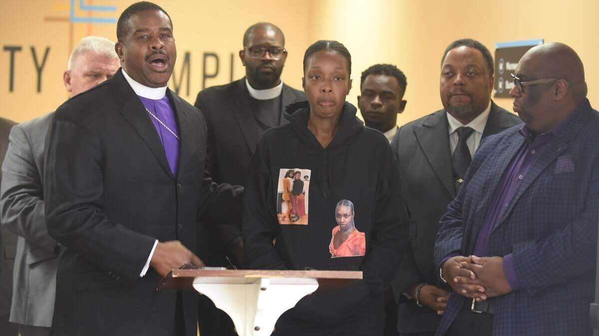 Aisha Johnson, center, whose 23-year-old daughter Era’Shae was fatally shot in Kansas City on Oct. 17, stands as Bishop Ben Stephens, left, and other Black faith leaders address area violence affecting women during a press conference in the Trinity Temple Church of God in Christ in Grandview on Thursday.
