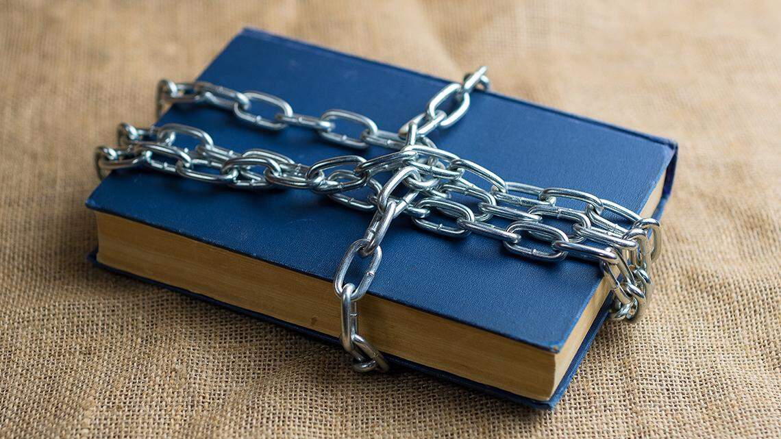 top view of a book in a blue cover lying on burlap, the book is wrapped in a chain, a forbidden banned book read reading censor censorship